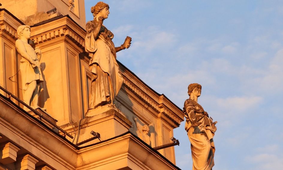  The image shows several statues of Greek gods and goddesses on the top of a building, the figures are intricately detailed and the overall composition is visually pleasing.
