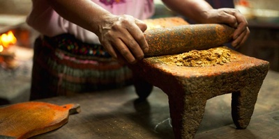 The woman is grinding chili for a sauce.