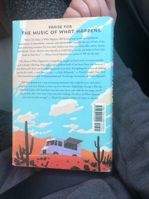 This photo shows the back of the book cover, it lists the description of the book. Firstly, it has a beautiful continued painting. The main focus being the clouds and great blue sky. There are sand dunes in the background and in the midground is a food truck with it's window open to serve. In the front ground shows more orange sand with tall grown cacti that equally space themselves as to not cover our view of the truck. The book's description reads: PRAISE FOR THE MUSIC OF WHAT HAPPENS “With The Music of What Happens, Bill Konigsberg serves up a profound examination of masculinity, consent, and relationships through the eyes of two of the most endearing narrators I've ever read. Jordan and Max are vulnerable, sweet, funny, and flawed. Teens, whether they identify as LGBTQIA+ or not, are lucky to have this book in their lives” -Shaun David Hutchinson, author of We Are the Ants “The Music of What Happens is a compelling, laugh-out-loud story, as swoon-worthy as it is deeply affecting. Max and Jordan grabbed hold of my heart from the moment I met them and I don't see them letting go any time soon. Konigsberg has a way of making me see the world- and food trucks!- a little differently.” -David Arnold, New York Times bestselling author of Mosquitoland and The Strange Fascinations of Noah Hypnotik “'Bill Konigsberg has a way of creating characters that could be your next-door neighbor, your best friend, or that cute boy who once helped you change a flat tire. Max and Jordan will find their way into your heart, and after the last page, you'll regret that they aren't real. Once you start reading The Music of What Happens, you won't be able to stop.” -Brigid Kemmerer, author of Letters to the Lost